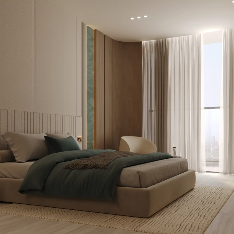 A modern bedroom at Binghatti Aquarise features a low beige bed, dark green bedding, light wood floors, a soft rug, small nightstand, white chair, large windows with sheer curtains, and neutral-toned walls bathed in natural light.