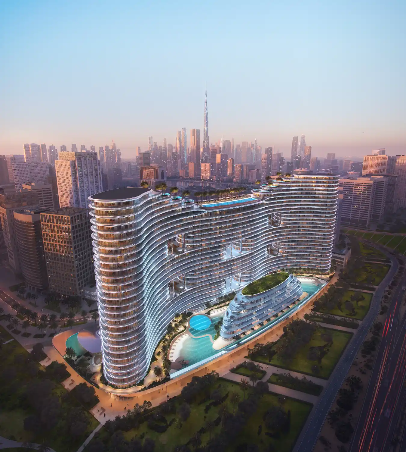 A futuristic, wavy glass building—Binghatti Aquarise—with illuminated edges stands amid greenery and pools, surrounded by city skyscrapers at sunset, with the Burj Khalifa visible in the distant skyline.