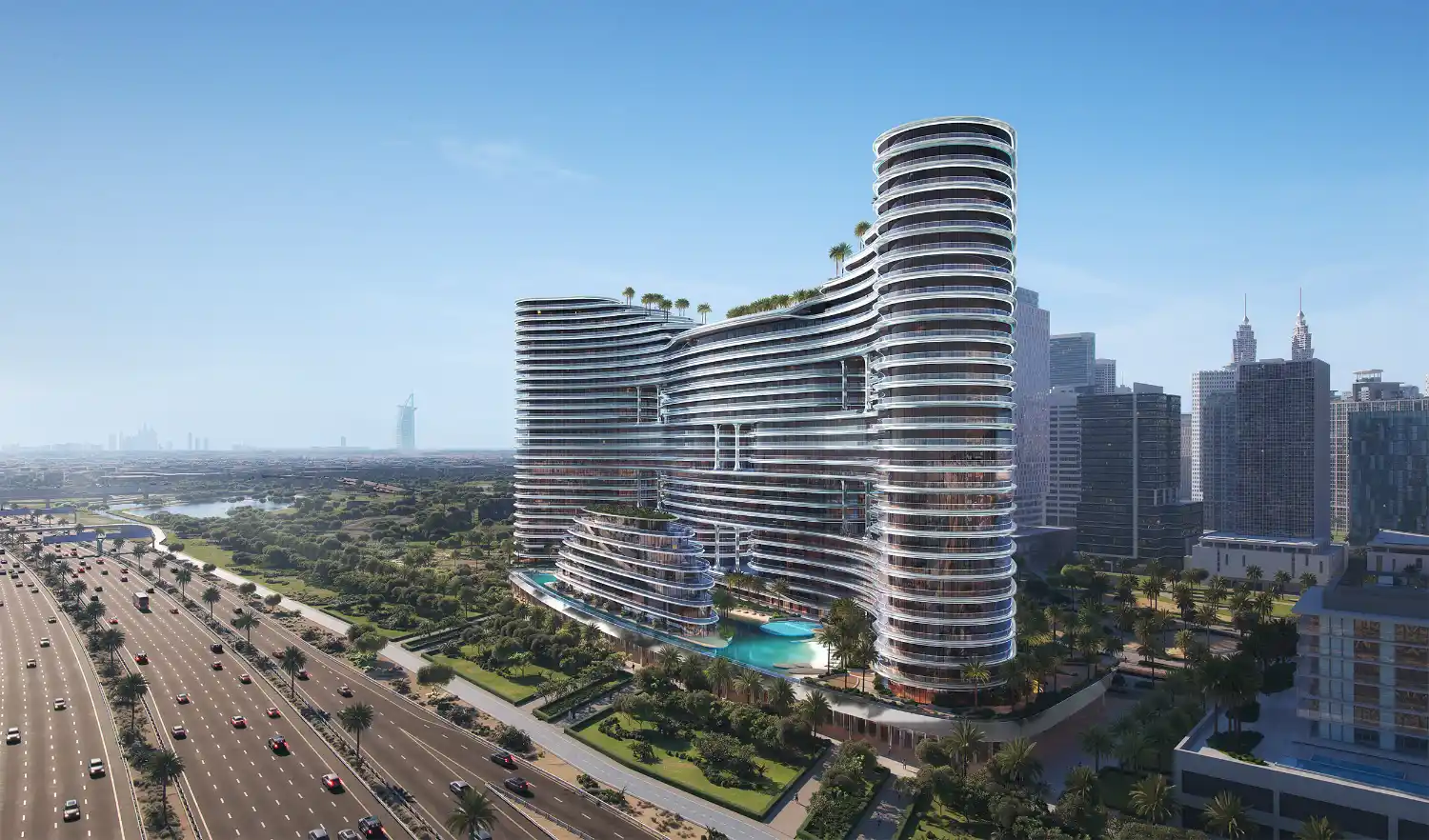 A modern, glass-clad high-rise with curved architecture—Binghatti Aquarise—features rooftop greenery and stands beside a busy multi-lane highway, surrounded by trees and cityscape under a clear blue sky.