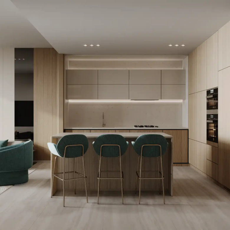 Modern kitchen with light wood cabinets, a central island with three teal barstools, built-in ovens, and minimalistic decor—reflecting the elegant style of Binghatti Aquarise. Open living area with teal sofa on the left. Soft, neutral tones throughout.