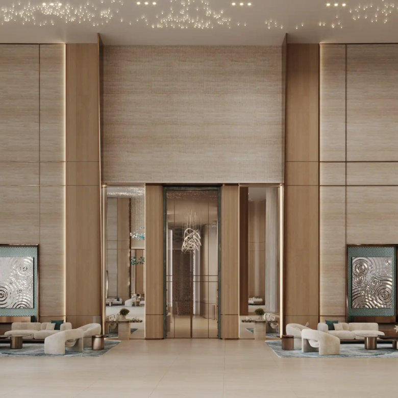 A spacious, modern lobby with tall wood-paneled walls at Binghatti Aquarise, featuring two symmetrical seating areas with white sofas, large decorative art pieces, potted trees, and a high ceiling adorned with small hanging lights.