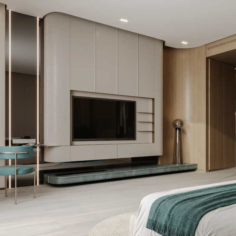 Modern bedroom at Binghatti Aquarise with built-in TV wall unit, teal accent chair at a small desk, wood paneling, and a neatly made bed with green accents. The space is minimalistic and well-lit.