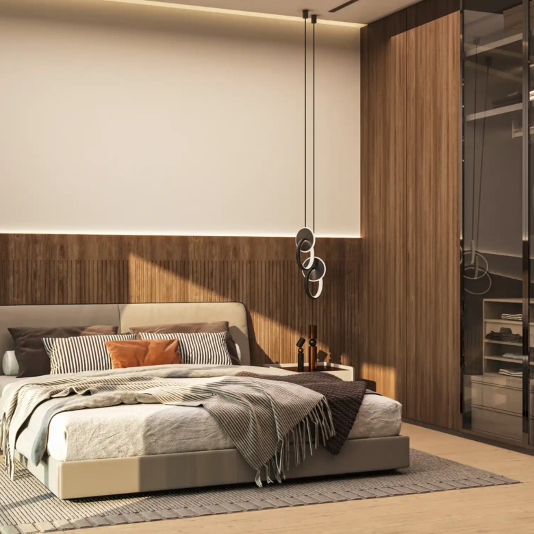 Modern bedroom at Binghatti Apex with a low bed, gray bedding, and decorative pillows. Wooden accent wall, built-in wardrobe with glass doors, pendant lights, and a small plant by the window create a warm, minimalist atmosphere.